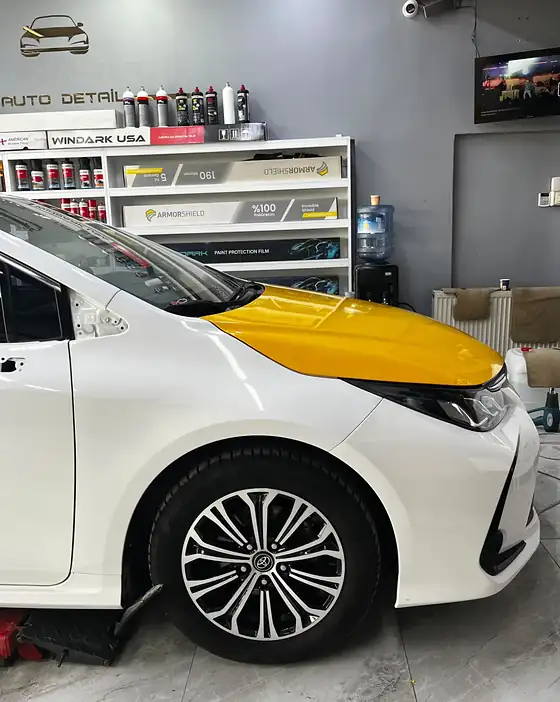 Beyaz Toyota Corolla'nın kaputu taksi sarısına kaplanmış, uygulama sürüyor